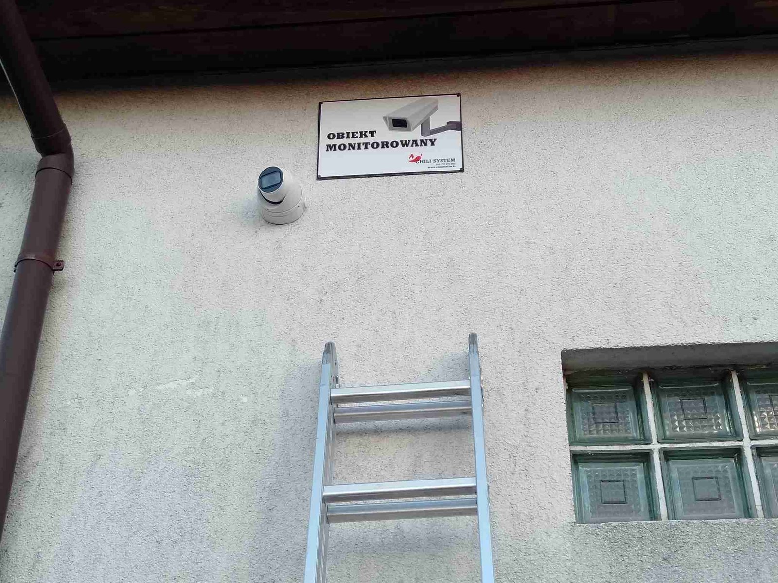 Kamera monitoringu i tabliczka Obiekt monitorowany na ścianie budynku firmy, Chili System